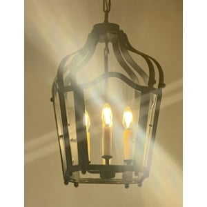 A stylish wrought iron pendant featuring a classic design with three candle-like bulbs. The fixture emits a warm glow, enhancing any interior space.