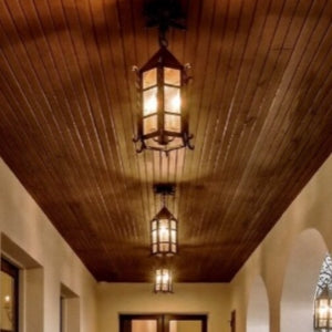 Three elegantly designed wrought iron fixtures hang from a wooden ceiling, casting a warm glow. Their intricate detailing and open-frame structure enhance the inviting atmosphere of the space. Perfect for adding a touch of rustic charm, these fixtures beautifully illuminate the area below.