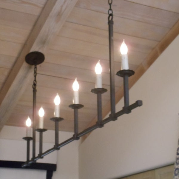 A sleek wrought iron chandelier featuring seven candle-style bulbs, suspended from a wooden ceiling with rustic beams, illuminating the space with warm, inviting light.