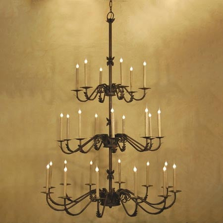 A large, elegant wrought iron chandelier featuring multiple tiers of candle-like lights. The intricate design includes curling arms and decorative details, creating a warm and inviting ambiance perfect for grand spaces.