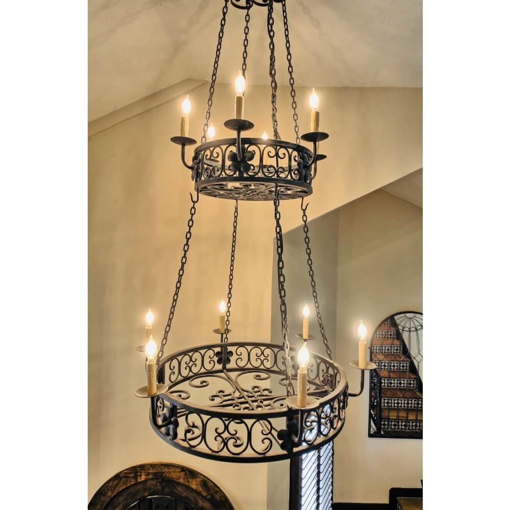 A stunning wrought iron chandelier featuring intricate scrolling designs, illuminated by multiple candle-style lights. It hangs gracefully from a chain, providing an elegant touch to any space.