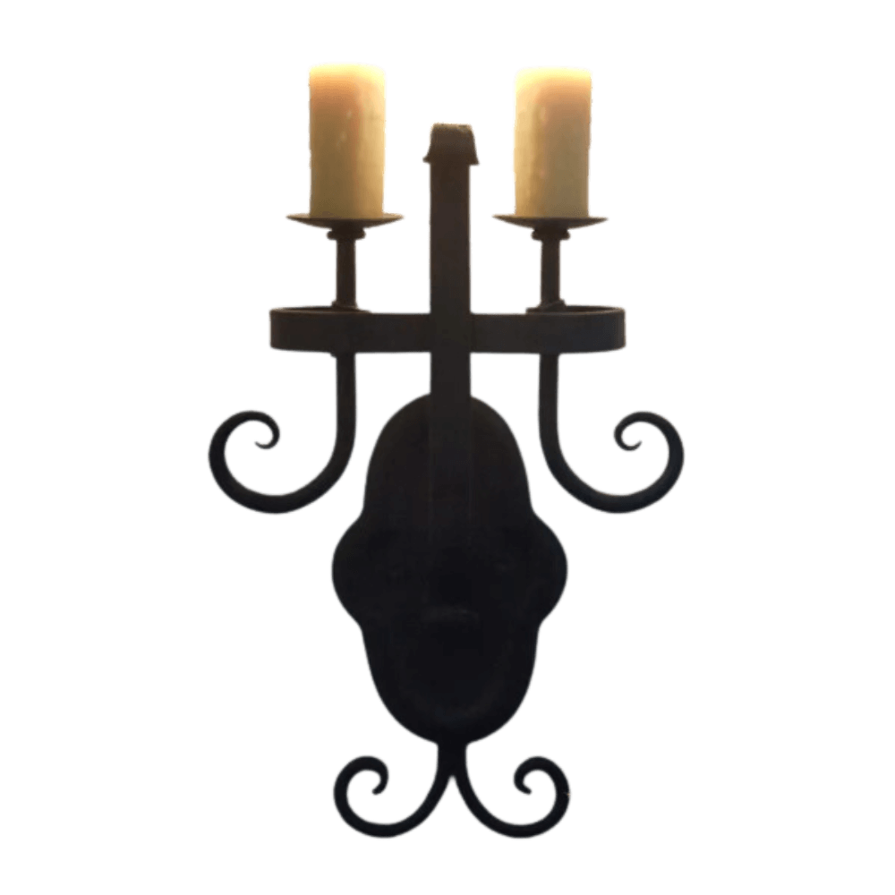 A decorative wall sconce featuring an ornate design with two candle-like fixtures atop a beautifully crafted base. The dark metal finish and elegant curves add a touch of vintage charm to any space, perfect for enhancing the ambiance.