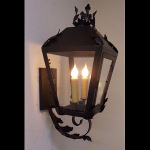 A beautifully crafted wrought iron sconce featuring intricate leaf motifs and a lantern-like design. It holds two candle-style lights, casting a warm glow through its clear panels, adding elegance and charm to any space.