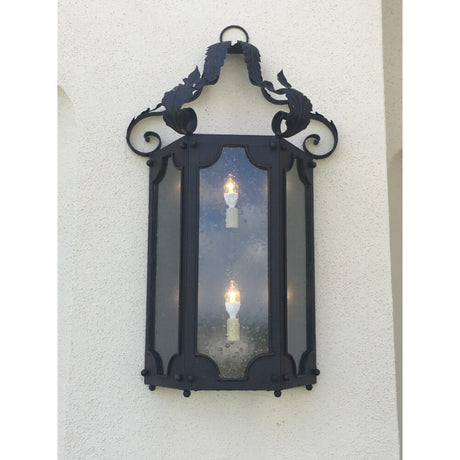 A decorative wall sconce featuring a wrought iron frame with elegant scrollwork and leaf motifs. The design showcases three candle-like lights within clear glass panels, providing a warm ambiance. Perfect for adding charm to entryways or outdoor spaces.