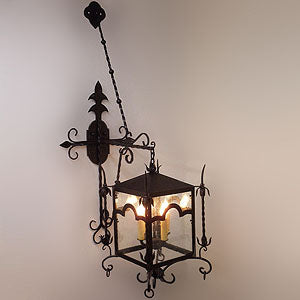 A decorative wrought iron wall sconce featuring intricate scrollwork and a glass enclosure, showcasing three candle-style lights. Ideal for adding elegance to any space.