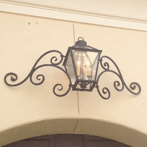 A decorative wrought iron wall sconce featuring a classic lantern design with intricate swirling elements and a warm glow from exposed bulbs.