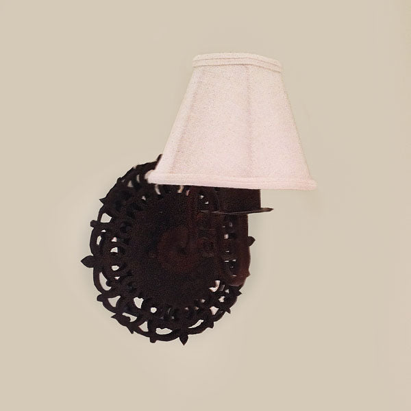 A beautifully crafted wall sconce featuring an intricate wrought iron backplate with decorative scrollwork, complemented by a soft, white fabric shade. This fixture adds warmth and elegance to any space.