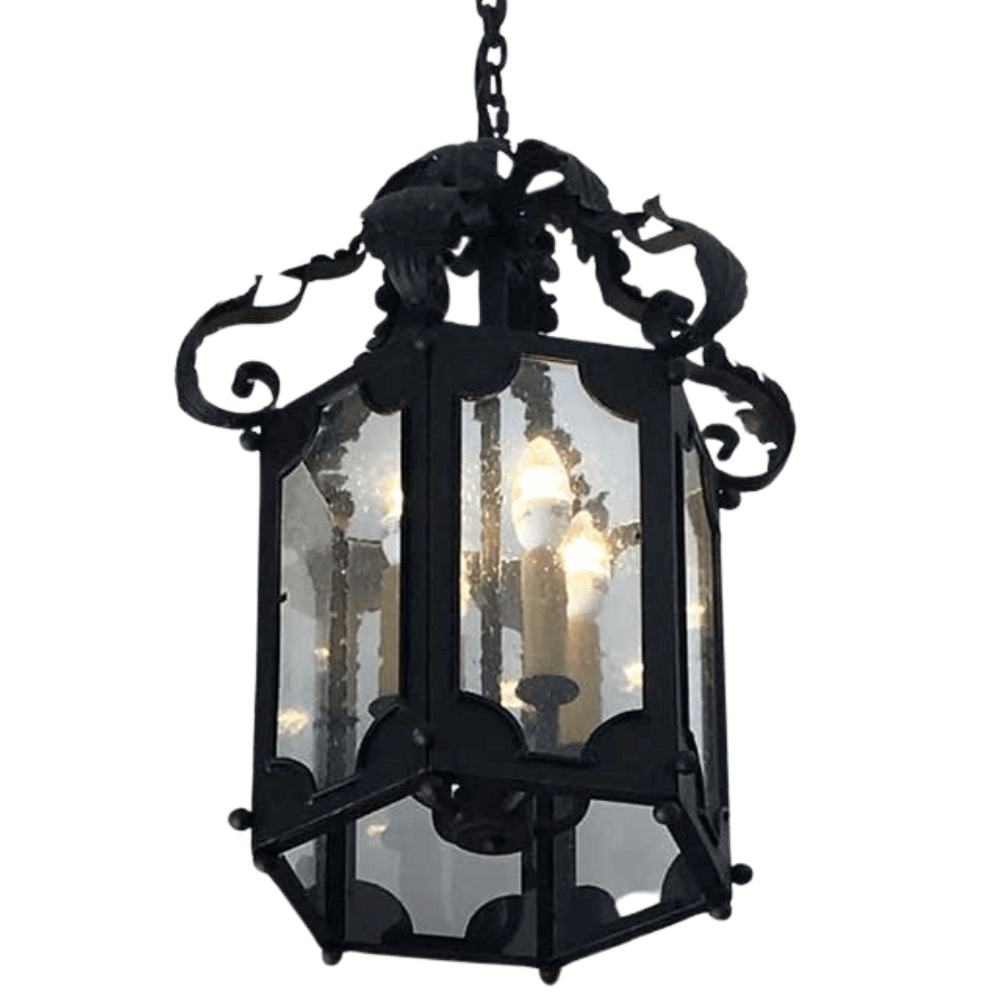 A beautifully crafted wrought iron pendant featuring intricate scrollwork and an octagonal design. The fixture showcases clear glass panels, illuminating the interior with soft light from candle-style bulbs.