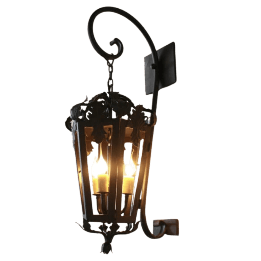 A decorative wrought iron wall sconce featuring intricate scrollwork and vine-inspired details. It houses three glowing bulbs, casting a warm ambiance, ideal for any rustic or traditional setting.