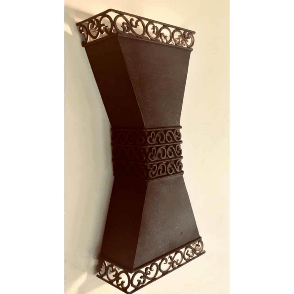 A uniquely designed wall sconce featuring a slender, hourglass shape with a decorative wrought iron top and intricate scrollwork. Its dark finish adds a touch of elegance, making it a stylish accent for various interiors.