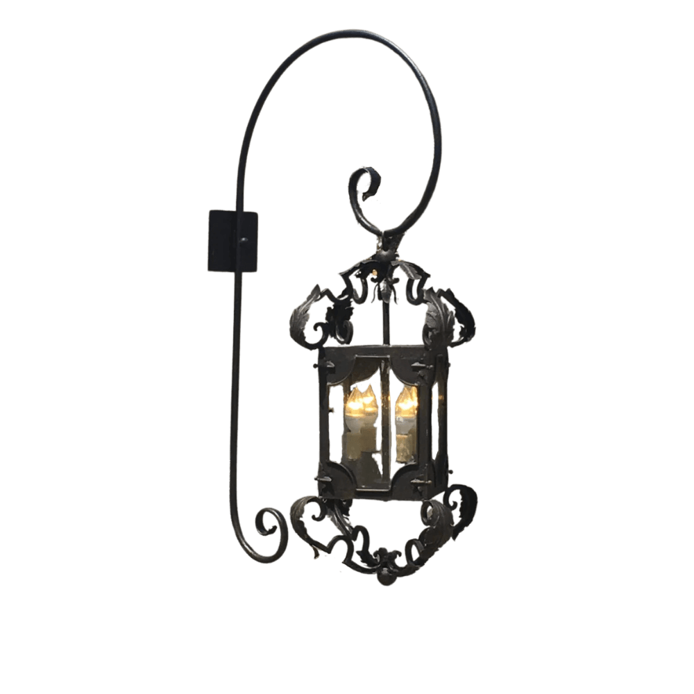 A decorative wall sconce featuring ornate wrought iron design with scrollwork details and a lantern-style housing. The fixture holds two candle-like bulbs, providing a warm glow. Ideal for enhancing traditional or rustic interiors.