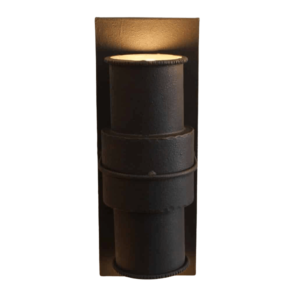 A stylish wrought iron wall sconce featuring a cylindrical design with textured surfaces and an elegant ring detail. The warm light casts a welcoming glow, enhancing any decor.