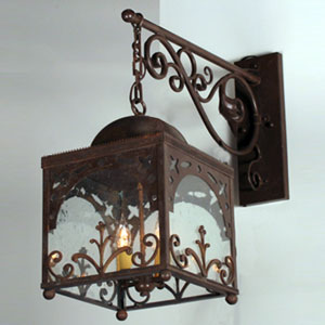 A beautifully crafted wrought iron wall sconce featuring intricate scrollwork and a glass enclosure, illuminating a warm glow through ornate designs.