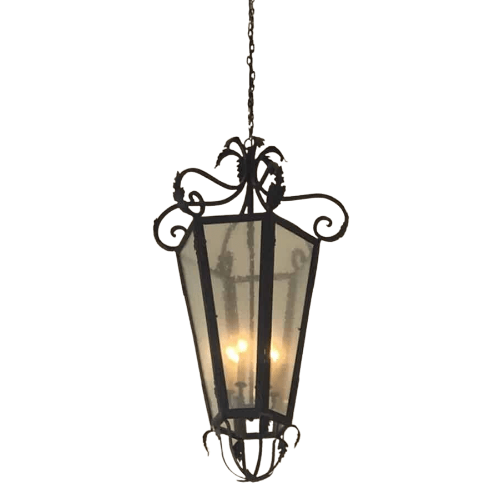 A beautifully crafted wrought iron pendant featuring an elegant, lantern-like design with ornate scrollwork and a glass enclosure. The interior lights create a warm glow, enhancing its decorative appeal.