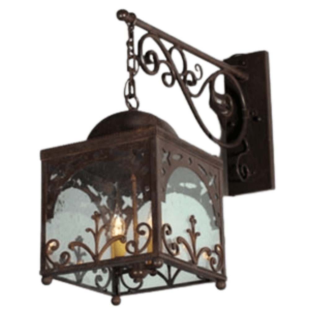 A wrought iron sconce features intricate scrollwork and a square glass enclosure, casting a warm glow from inner candle-like bulbs.