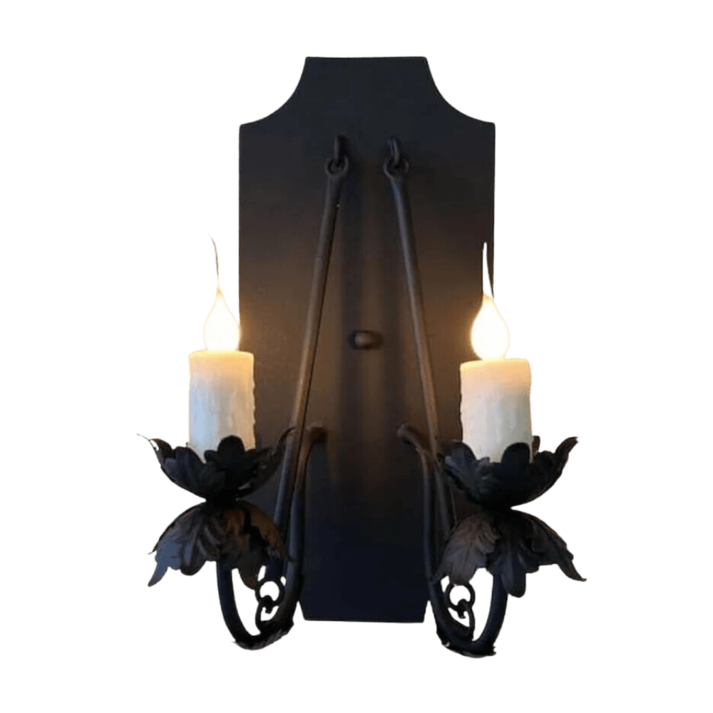 A decorative wrought iron sconce featuring two candleholders embellished with leaf motifs, radiating a warm glow.