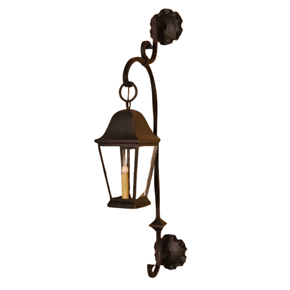 A decorative wrought iron sconce featuring a candle-like bulb within a classic lantern design. The fixture has elegant curves and floral accents, enhancing its vintage charm, perfect for adding warmth to any space.