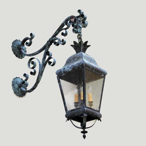 A decorative wall sconce featuring ornate scrollwork and a detailed lantern design. The fixture is finished in a weathered patina, beautifully illuminating outdoor spaces.