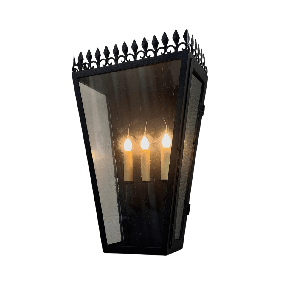 A striking wrought iron sconce featuring three candle-style bulbs inside a glass enclosure. The design includes an ornate pointed crown and an elegant, vintage-inspired aesthetic, perfect for enhancing any space with warm, inviting light.
