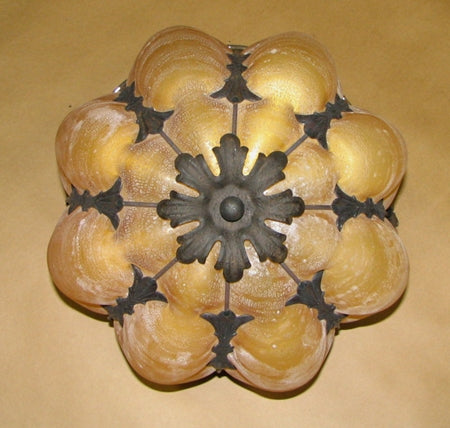 Elaborate wrought iron fixture features a floral design with a warm amber shade. The intricate black metalwork complements the soft glow, ideal for elegant spaces. Perfect for adding character and charm.