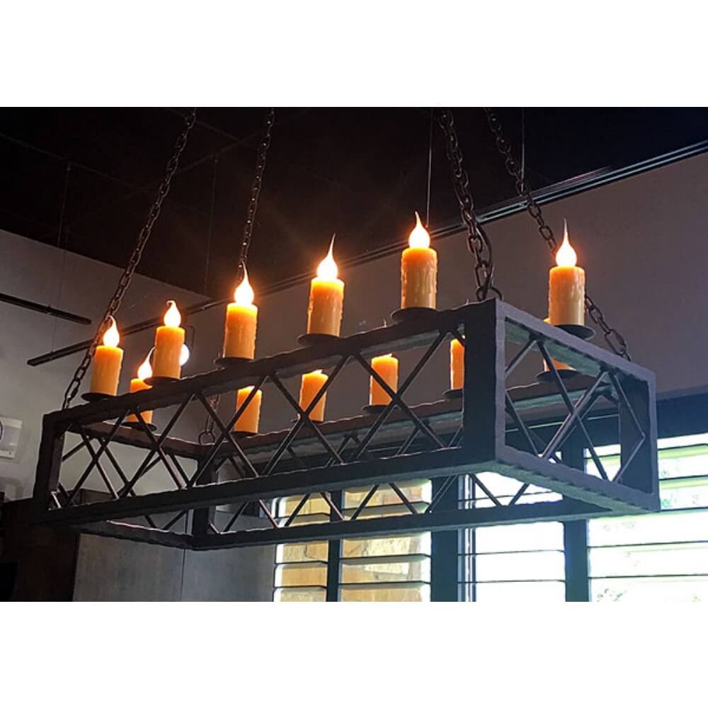 A rectangular chandelier with eight flickering candle lights, suspended by chains. The fixture features intricate wrought iron detailing, enhancing its rustic aesthetic.
