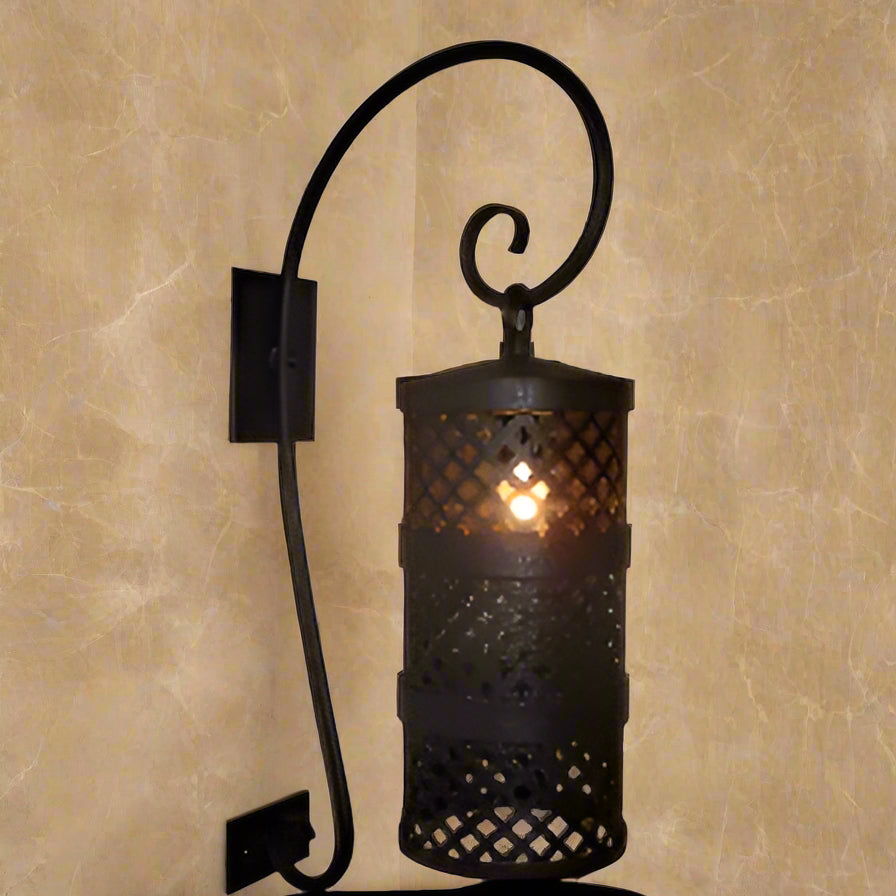 A decorative wrought iron wall sconce featuring intricate latticework and a cylindrical shade. The design includes a graceful scroll arm, providing both style and illumination to any space.