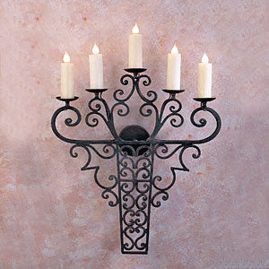 A decorative wall sconce featuring intricate wrought iron design with swirling patterns and five candle holders, complementing various indoor aesthetics.