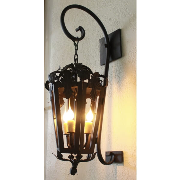 A decorative wrought iron sconce featuring intricate leaf designs, illuminating three candles. The elegant curves and detailed craftsmanship enhance any interior space.