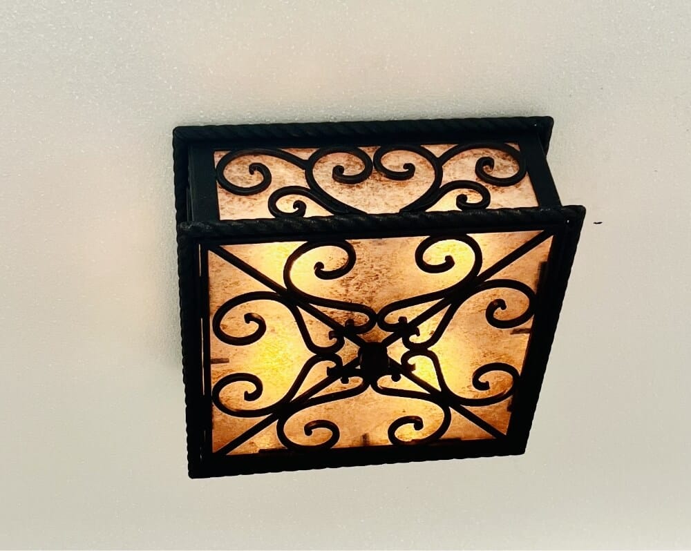 A decorative ceiling fixture featuring intricate wrought iron scrollwork and a warm amber glow, perfect for enhancing any rustic or vintage-inspired space.