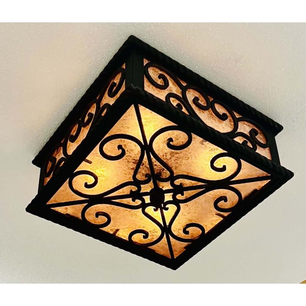 A decorative wrought iron ceiling fixture featuring intricate swirling designs and warm-toned glass panels, providing soft ambient lighting.