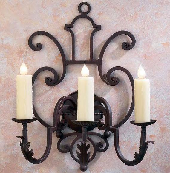 A decorative wall sconce featuring three elegantly curved arms and subtle floral accents, each holding a tall, creamy candle. The intricate wrought iron design combines artistry and functionality, perfect for adding warmth and sophistication to any room.