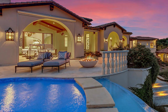 A beautifully designed outdoor space featuring a pool, lounge chairs, and a fire pit. Elegant wrought iron sconces illuminate the archways of a stylish home, showcasing intricate detailing.
