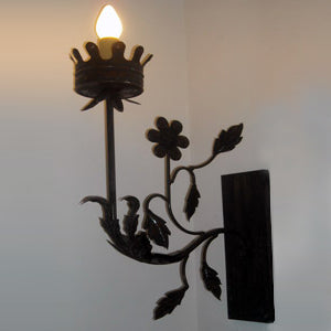A beautifully crafted wall sconce featuring intricate floral and leaf designs, with a charming crown-shaped holder for a warm light bulb. The wrought iron construction adds an elegant touch, making it a perfect accent for any room.