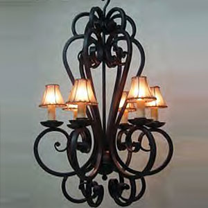 A gracefully designed chandelier featuring intricate wrought iron scrollwork and six elegant lamp shades, providing warm ambient light.