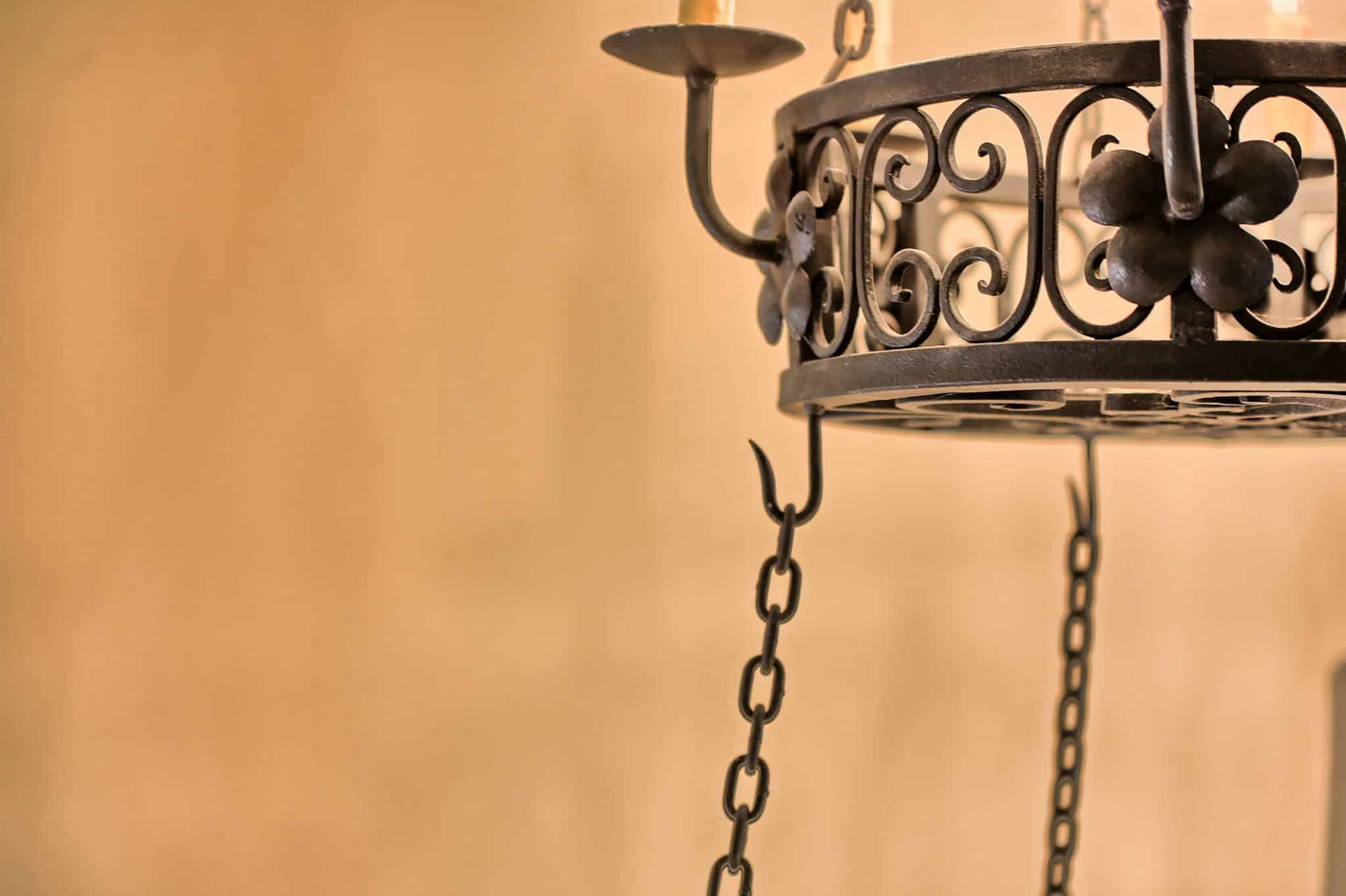 A beautifully crafted wrought iron chandelier features intricate scrollwork and floral accents. Suspended by chains, it elegantly holds multiple candle-like lights, perfect for adding warmth and charm to any space.