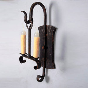 Elegant wrought iron sconce featuring two candle-style lights, set against a textured backplate. The intricate design and rich finish add a warm, inviting ambiance to any space.