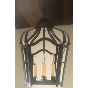 A beautifully crafted wrought iron pendant light featuring an ornate design. It has three candle-style bulbs with textured, cream-colored bases. The fixture's elegant curves and intricate detailing create a warm, inviting atmosphere, perfect for enhancing any space.