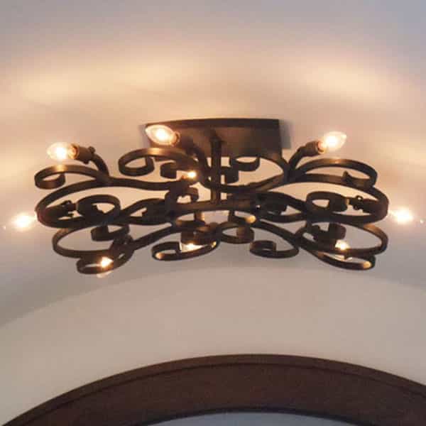 A decorative ceiling fixture made of intricate wrought iron, featuring swirling, organic shapes and multiple light bulbs, casting a warm glow.