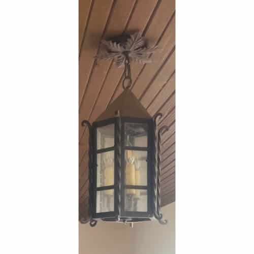 A beautifully crafted wrought iron pendant featuring a hexagonal glass enclosure, adorned with ornate scrollwork and a decorative finial. This piece combines elegance and rustic charm, perfect for enhancing any space.