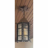 A beautifully crafted wrought iron pendant featuring a hexagonal glass enclosure, adorned with ornate scrollwork and a decorative finial. This piece combines elegance and rustic charm, perfect for enhancing any space.