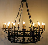A large wrought iron chandelier featuring intricate scrollwork and candle-like lights. It hangs from a sturdy chain and provides an elegant, warm glow.