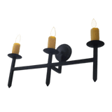 A sleek wrought iron sconce featuring three candle holders with warm, flickering flames, and a minimalist design. Ideal for adding a rustic yet elegant touch to any space.