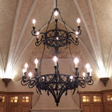 A large, intricately designed wrought iron chandelier hangs from a vaulted ceiling, showcasing ornate curves and elegantly positioned lights. The warm glow illuminates the sophisticated space, complementing the rich wooden cabinetry below.