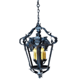 A beautifully crafted pendant featuring ornate wrought iron detailing and three candle-style lights. The design incorporates intricate curves and floral accents, adding elegance to any space.