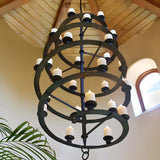 A striking wrought iron chandelier featuring multiple circular tiers adorned with candle-like lights, suspended from a wooden ceiling, adding elegance to the space.