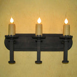 A sleek wrought iron wall sconce featuring three candle holders with warm, flickering LED lights, mounted against a textured yellow wall. The elegant design showcases ornate details and sturdy craftsmanship, enhancing any interior with a touch of sophistication.