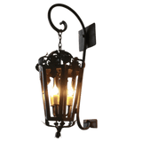 A decorative wrought iron wall sconce featuring intricate scrollwork and vine-inspired details. It houses three glowing bulbs, casting a warm ambiance, ideal for any rustic or traditional setting.