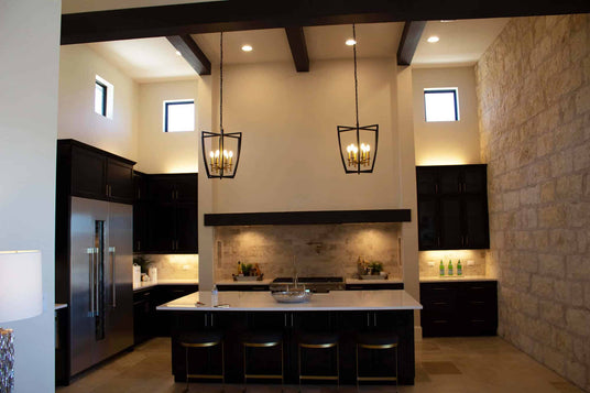 Stylish kitchen featuring two elegant wrought iron pendants with warm lighting suspended above a modern island. The space showcases dark cabinetry and a natural stone wall, creating a sophisticated atmosphere.