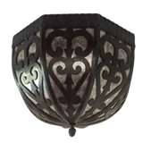 A beautifully crafted wrought iron sconce featuring intricate, swirling designs. The dark metalwork contrasts elegantly with the muted light filtering through, creating a warm and inviting glow. This fixture adds a touch of rustic charm and artistic flair to any interior space.