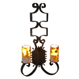 A decorative wall sconce featuring an elegant wrought iron design with flowing curves and stylized scrollwork. It has two candle-like lights with amber and gray hues, providing a warm, inviting glow.